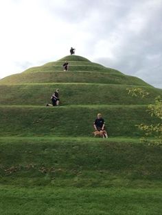 three people sitting on the top of a grassy hill with stairs leading up to them