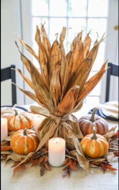 an arrangement of pumpkins and gourds on a dining room table with candles