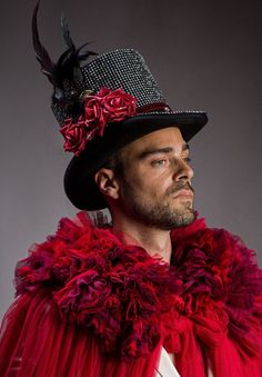 a man wearing a red dress and hat with feathers