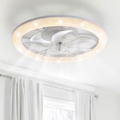 a white ceiling fan with lights on it in a room next to curtains and windows