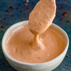 a spoon dipping some kind of sauce into a small white bowl on a blue surface