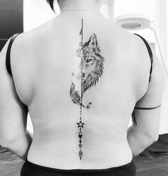 a woman's back with a wolf and arrow tattoo on her left side ribcage