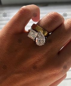 a person's hand holding a ring with two diamonds on it and the middle finger