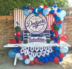 a table with balloons and decorations for a dodgers baseball birthday party on the side of a brick wall