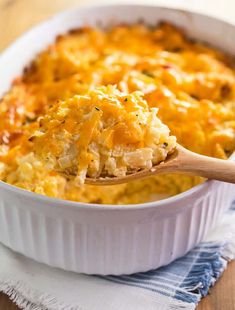 a casserole dish with chicken and cheese in it on a blue towel next to a wooden spoon