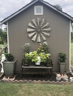 a garden shed with potted plants on the side and a windmill decoration above it