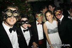 a group of people standing next to each other in front of a christmas tree wearing masks