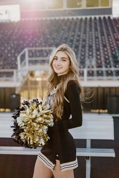 a beautiful young woman holding a cheerleader's pom - pom in front of a football stadium