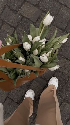 a person holding a bouquet of white tulips in their hands on the ground