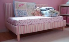 a teddy bear sitting on top of a pink bed next to pillows and blankets in a child's room