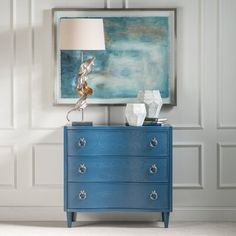 a blue chest of drawers with a lamp and painting on the wall in front of it