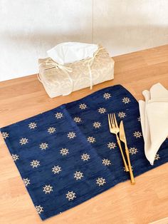 a place mat, fork and napkins on a wooden table with a white bag in the background