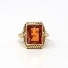 Beautiful vintage circa 1940s Retro era created orange sapphire ring! This pretty ring features a rectangular faceted 3.95 carat created orange sapphire stone, that is securely bezel set. The piece has a stylish setting with sweet floral shoulders. A gorgeous piece of fine retro jewelry, featuring a stunning bright orange stone! ERA - Circa 1940s - Retro METAL / MATERIAL - 10k yellow gold, created orange sapphire (approx. 3.95 CT)  MARKINGS / HISTORY - Inside of the band is marked 10k CONDITION - Good vintage condition. Yellow gold metal has been professionally polished & cleaned. Created orange sapphire is securely set. Some tarnish wear remains. Amazing vintage created orange sapphire ring!  SIZE / MEASUREMENTS - Size: 3, Ring Head Height: 14 mm, Back of Shank: 1.6 mm, Created Orange Sap Retro Orange Jewelry For Formal Events, Retro Orange Jewelry For Formal Occasions, Retro 14k Gold Ring For Gift, Retro 14k Gold Ring As Gift, Vintage Orange Rings For Formal Occasions, Retro 14k Gold Rings As Gift, Orange Vintage Rings For Formal Occasions, Vintage Gold Ring With Rectangular Stone, Vintage Gold Octagon Jewelry