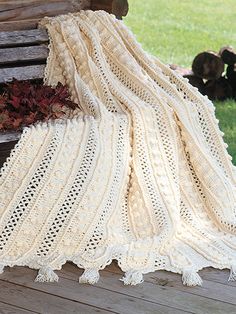 a white crocheted blanket sitting on top of a wooden bench next to flowers