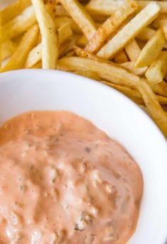 a white bowl filled with dipping sauce next to french fries and ketchup on the side