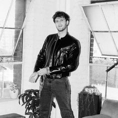 black and white photograph of a man standing in front of a window with his hands in his pockets