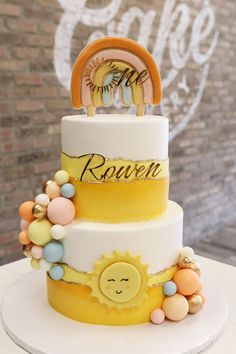 a three tiered cake with sun and moon decorations on the top, sitting on a table in front of a brick wall