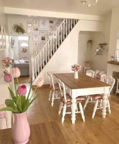 a dining room table and chairs with pink flowers in the vase on the floor next to it