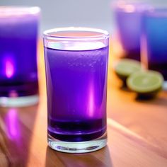 two glasses filled with purple liquid sitting on top of a wooden table next to lime slices