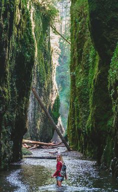 a woman wading through a river surrounded by mossy cliffs