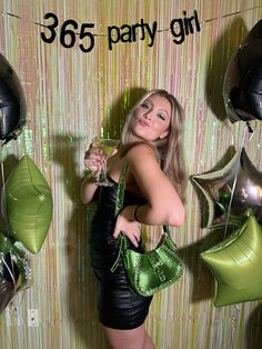 a woman posing in front of balloons and holding a green purse