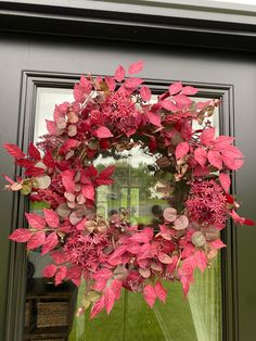 a wreath hanging on the front door of a house with pink flowers and green leaves