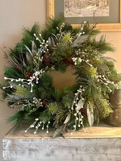 a wreath with white berries and pine cones on top of a mantle in front of a painting