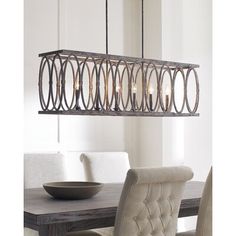 a chandelier hanging over a dining room table with chairs and a bowl on it