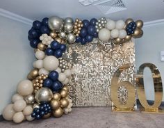 the balloon arch is decorated with gold, silver and blue balloons that spell out 60