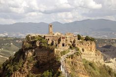 an old building on top of a cliff with mountains in the background and clouds overhead