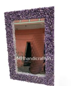 a mirror made out of purple rocks with the reflection of a building on it's side