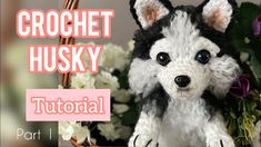 a crochet husky dog sitting in front of a basket with flowers and greenery