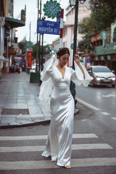 a woman in a white dress crossing the street with an angel wings on her head