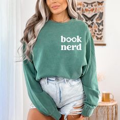 a woman wearing a green sweatshirt with the words book nerd printed on it in white