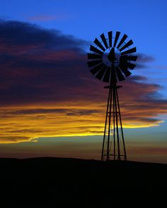 a windmill sitting on top of a hill under a cloudy blue and orange sky at sunset