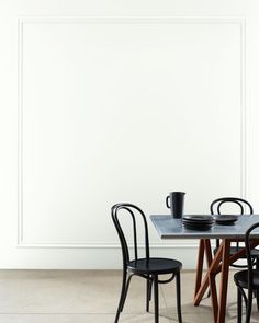 two chairs and a table in front of a white wall with a black cup on it