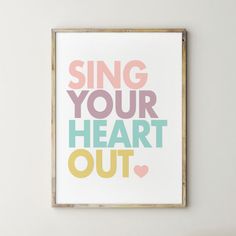 a framed print with the words sing your heart out in multicolored letters on a white wall