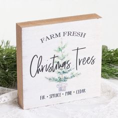 a christmas tree sign sitting on top of a white lace table cloth next to evergreen branches