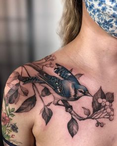 a woman's chest with a blue bird on it and flowers around her neck