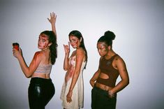 three young women standing next to each other in front of a white wall with their hands up