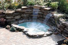 an outdoor hot tub surrounded by rocks and water features a waterfall that flows into the pool