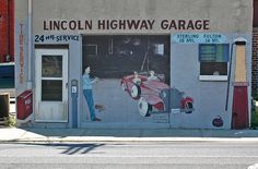 a mural on the side of a building depicting a man repairing a car in front of it