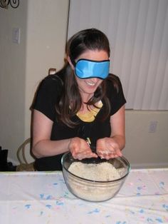 a woman wearing blindfolds making food in a bowl on top of a table