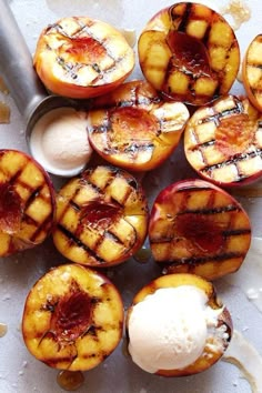 grilled peaches and ice cream on a white surface with spoons next to them