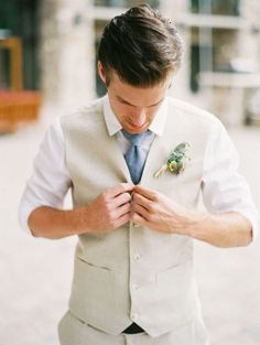 a man in a white suit and tie is looking down at his pocket square shirt