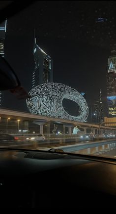 the view from inside a car at night with buildings in the background and lights on