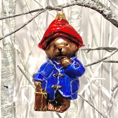 a bear ornament hanging on a tree branch in front of snow covered trees