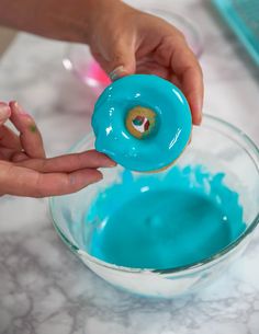 a person is sprinkling blue icing on a doughnut in a glass bowl