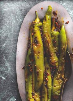 a white plate topped with green beans covered in seasoning next to a silver spoon