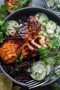 a bowl filled with black rice, cucumber and salmon on top of it